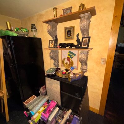 Sale Photo Thumbnail #120: Collection of Egyptian-themed home decor displayed on decorative corbel wall shelves and a small cabinet, alongside various boxed items on the floor.