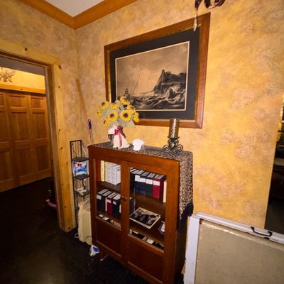 Sale Photo Thumbnail #121: Vintage mid-century wooden glass-door bookcase cabinet topped with decor, beneath a framed seascape art print.