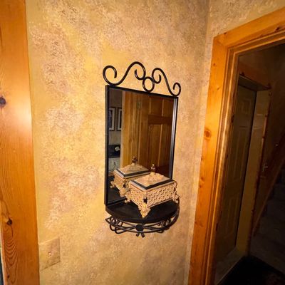 Sale Photo Thumbnail #85: Wrought iron wall-mounted mirror featuring scrollwork accents and a integrated shelf holding a decorative trinket box.