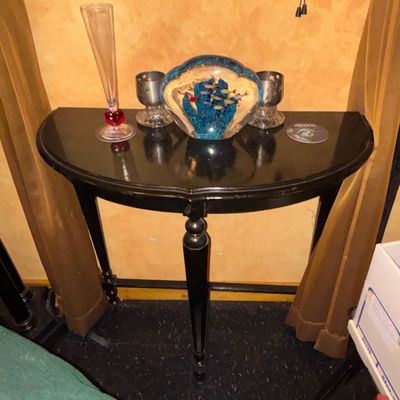 Sale Photo Thumbnail #94: Black painted half-moon console table with decorative items including a clear glass vase with a red heart accent, a seashell-shaped underwater paperweight, and two metal candle holders.