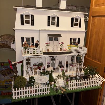 Sale Photo Thumbnail #124: Large, detailed three-story miniature dollhouse featuring white siding, black shutters, twin chimneys, and a fully furnished wraparound porch and landscaped yard.