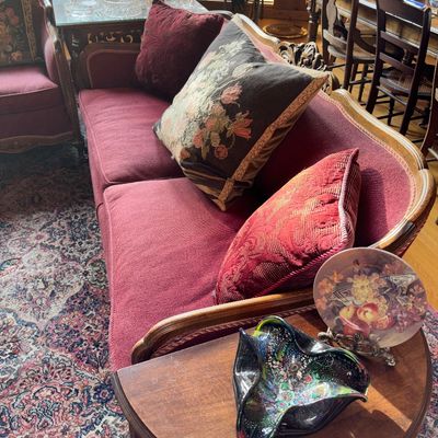 Sale Photo Thumbnail #77: French Provincial style sofa with burgundy upholstery and carved wood frame, displayed with patterned accent pillows and a wooden side table.
