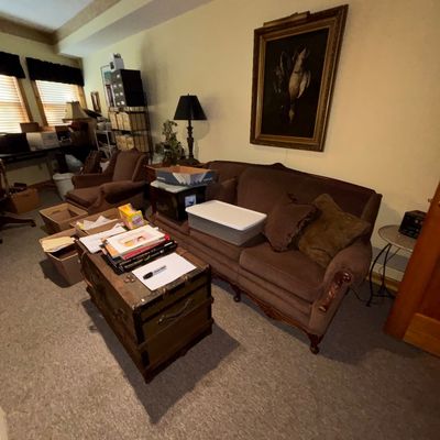 Sale Photo Thumbnail #28: Brown velvet upholstered camelback sofa with matching armchair, paired with an antique steamer trunk used as a coffee table and a framed still-life painting.
