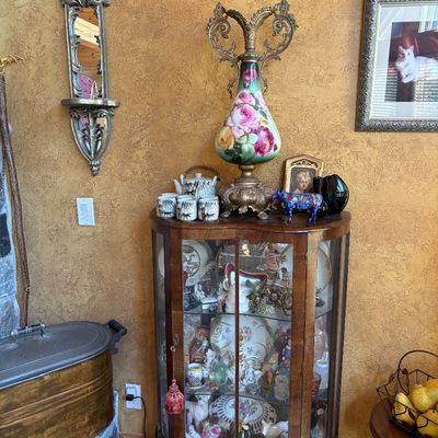 Sale Photo Thumbnail #66: Vintage wood and glass curio cabinet filled with collectibles, topped with an ornate floral painted table lamp and decorative tea set.