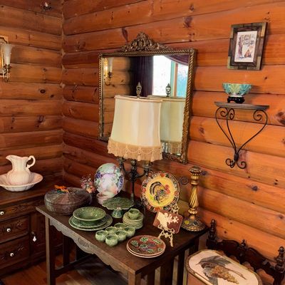 Sale Photo Thumbnail #54: Rustic wooden console table arranged with green ceramic tableware, decorative plates, a fringed lamp, and vintage home decor inside a log cabin interior.