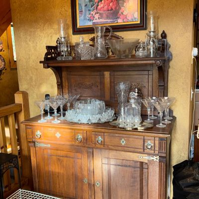 Sale Photo Thumbnail #51: Antique carved oak hutch with upper shelf display, holding an assortment of crystal glassware, pitchers, decanters, and cocktail glasses.