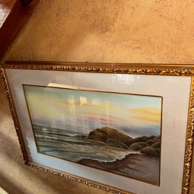 Sale Photo Thumbnail #36: Framed coastal seascape painting depicting waves crashing on a rocky shore at sunset, presented in an ornate gilded frame with a linen mat.