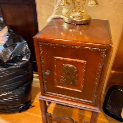 Sale Photo Thumbnail #34: Vintage carved wooden telephone cabinet with a carved profile medallion on the door, topped with a brass and cream French-style cradle telephone.