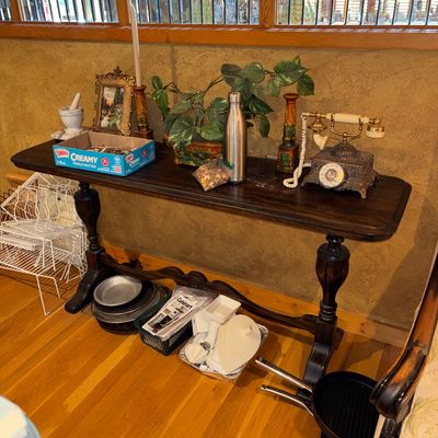 Sale Photo Thumbnail #7: Dark wood trestle console table displaying various home decor items, including an ornate vintage-style telephone, candle holders, and small framed art, with cookware and kitchen gadgets arranged underneath.