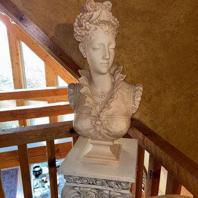 Sale Photo Thumbnail #47: Neoclassical-style alabaster or marble bust of an elegant woman with an ornate high hairstyle, mounted on a matching plinth pedestal.