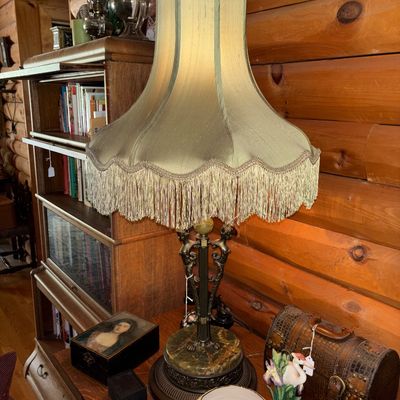 Sale Photo Thumbnail #9: Vintage ornate table lamp featuring a green marble base, cast metal figurative column, and a large scalloped fabric shade with fringe trim.
