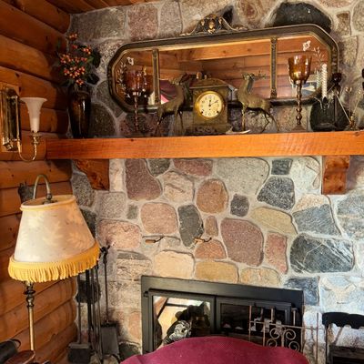 Sale Photo Thumbnail #53: Rustic stone fireplace mantel displaying a vintage mantel clock, brass deer figurines, amber glass candleholders, and a large ornate wall mirror above.