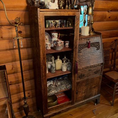 Sale Photo Thumbnail #11: Antique oak side-by-side secretary desk and curio cabinet featuring ornate carved detail, mirrored top shelf, and drop-front desk surface.