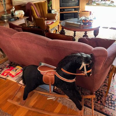 Sale Photo Thumbnail #55: Black plush rocking horse with leather saddle and bridle on a wooden glider base, displayed in a rustic living room setting.