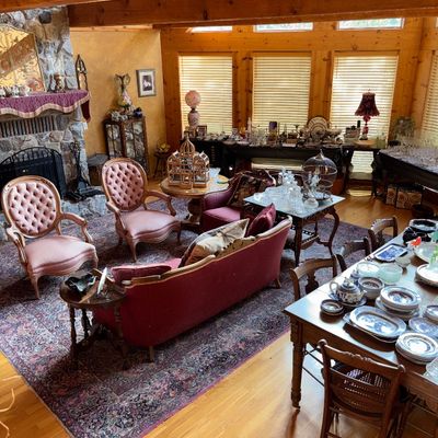 Sale Photo Thumbnail #40: Spacious living area featuring Victorian-style tufted armchairs, a burgundy sofa, an area rug, and tables displayed with glassware and chinaware.