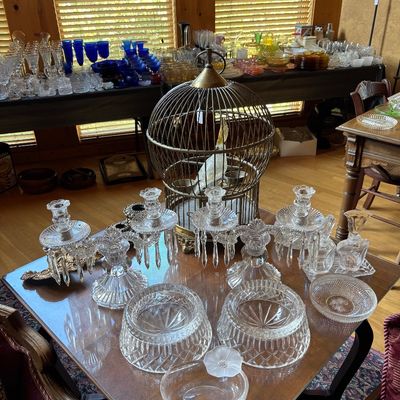 Sale Photo Thumbnail #128: Collection of crystal glassware, including prism candlesticks, bowls, and perfume bottles, displayed alongside a decorative brass birdcage with a fake bird.