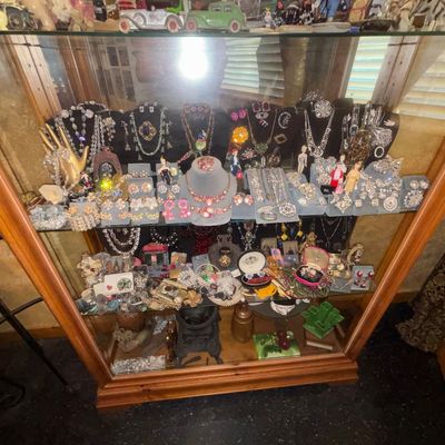 Sale Photo Thumbnail #2: Wooden display cabinet filled with vintage costume jewelry, including rhinestones, necklaces, earrings, and brooches, displayed on jewelry stands and trays.