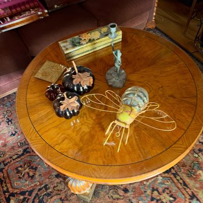 Sale Photo Thumbnail #52: Round wood pedestal coffee table featuring inlaid stringing detail, displaying decorative items including a metal insect light fixture, ceramic pumpkins, a floral box, and a figurine candlestick.