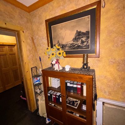 Sale Photo Thumbnail #4: Wooden display cabinet with glass doors filled with books, topped with decorative accents and a large framed seascape artwork hanging above.