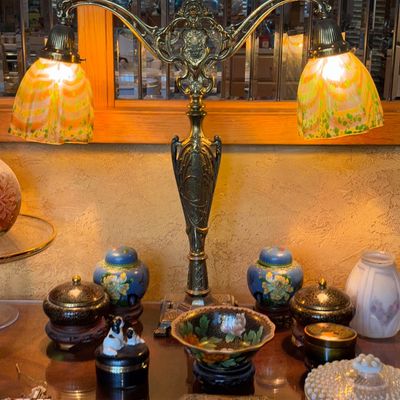 Sale Photo Thumbnail #12: Ornate double-light brass table lamp with Art Nouveau influence and marbled glass shades, surrounded by small decorative collectibles.