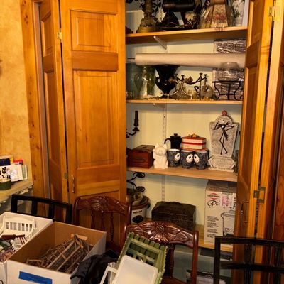Sale Photo Thumbnail #93: Closet packed with various home decor items, lamps, kitchenware, and Halloween collectibles, alongside dining chairs and storage boxes.