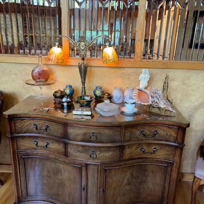 Sale Photo Thumbnail #17: Traditional serpentine mahogany credenza with brass hardware, displayed with an ornate double-arm table lamp and various decorative collectibles on a glass top.
