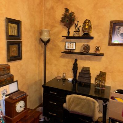 Sale Photo Thumbnail #110: Corner office setup featuring a black wooden desk with drawers, an Egyptian-themed decor collection including a King Tut bust and wall art, a torchiere floor lamp, and a vintage mantle clock.