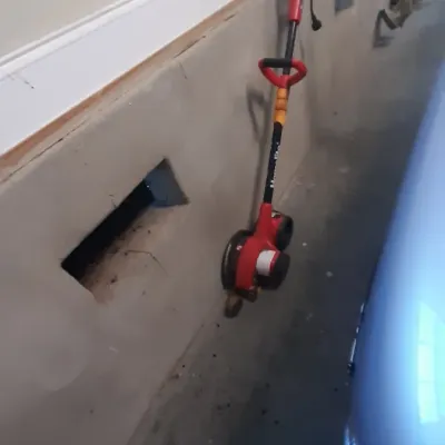 Red Homelite electric lawn edger leaning against a garage wall, showing light wear from use.
