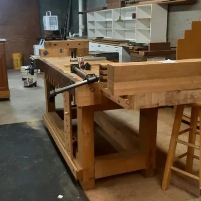 Large wooden joiner's workbench with built-in vise and dog holes, situated in a home workshop basement.