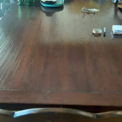 Large dark wood dining table featuring green glassware, serving dishes, and small household items displayed on top.