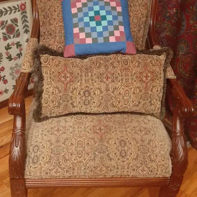 Traditional wooden armchair with carved details and patterned upholstery, paired with a matching lumbar pillow and a colorful patchwork...