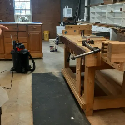 Large wooden joiner's workbench with integrated vises and dog holes in a basement workshop setting.