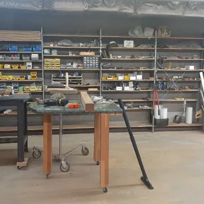 Workshop area featuring extensive metal shelving units stocked with hardware organizers, hand tools, supplies, and mobile worktables.