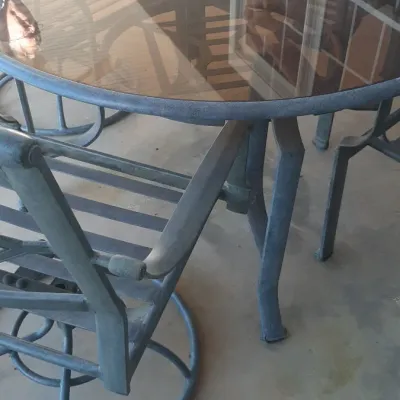 Outdoor patio dining set featuring a round glass-top table with metal frame and matching swivel rocker chairs.