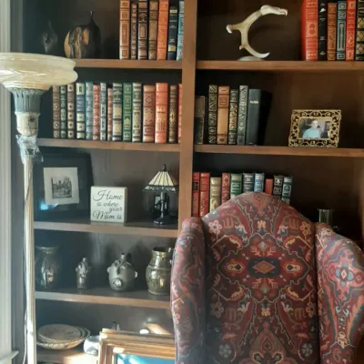 Large wooden built-in bookcase filled with vintage books, ceramics, and decorative objects, paired with a patterned tapestry wingback...
