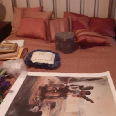 Traditional brass spindle bed set with a rust-colored quilt, decorative throw pillows, a heart-shaped box, and an unframed Western art...