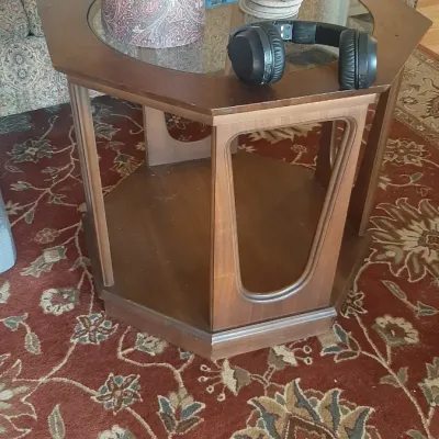 Mid-century modern style octagonal wooden side table with glass insert top, open-frame sides, and lower shelf, displaying miscellaneous...