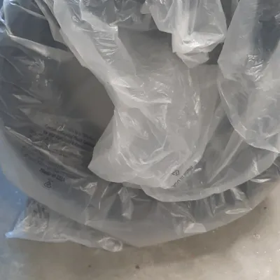 Vehicle tire wrapped in a protective clear plastic bag, sitting on a concrete floor.