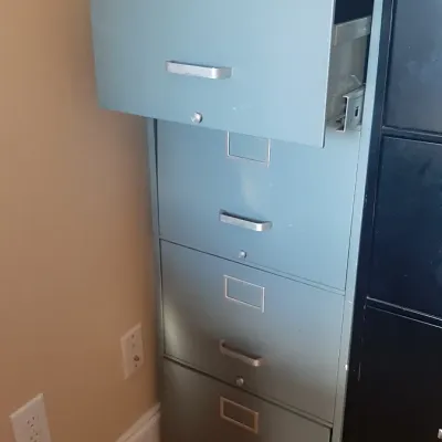 Vintage slate blue four-drawer metal filing cabinet with silver handles and label holders, shown with top drawer partially open.
