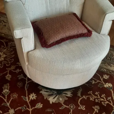Off-white upholstered barrel-style swivel armchair paired with a small patterned accent pillow.