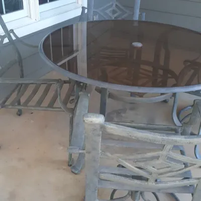Metal patio dining set featuring a glass-top table with umbrella hole and four matching swivel chairs with geometric lattice backs.