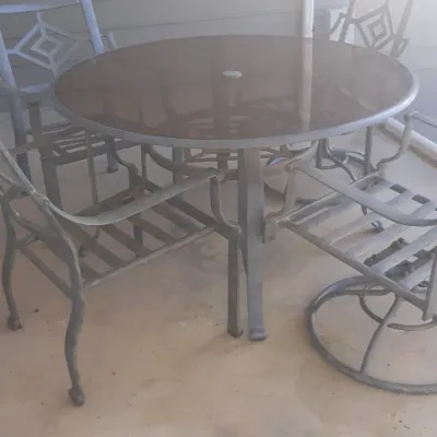 Outdoor patio dining set featuring a round glass-top metal table accompanied by four matching metal armchairs.