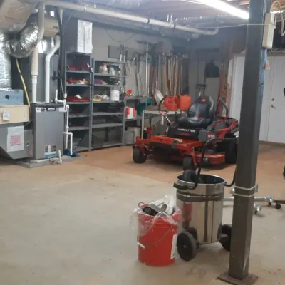 Workshop and storage area featuring a red Toro TimeCutter zero-turn riding lawn mower, shop vacuum, and wall shelving filled with tools...