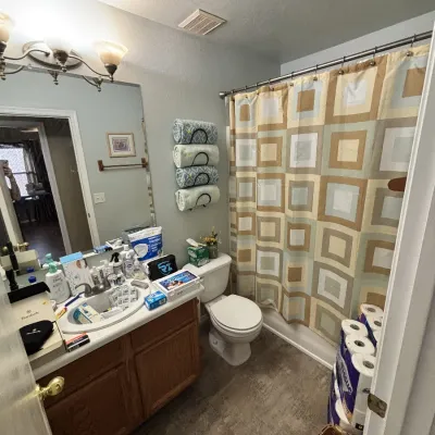 Sale Photo Thumbnail #14: Bathroom view featuring a vanity filled with assorted toiletries, a wall-mounted towel rack, a geometric shower curtain, and various household supplies.