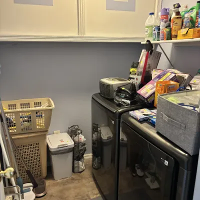 Sale Photo Thumbnail #28: Laundry room set featuring modern dark gray washer and dryer units, flanked by cleaning supplies, hampers, and small appliances.
