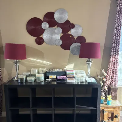 Sale Photo Thumbnail #37: Black eight-cube bookcase displays a large selection of CDs and media accessories, flanked by a pair of silver table lamps with red shades under a contemporary circular wall sculpture.
