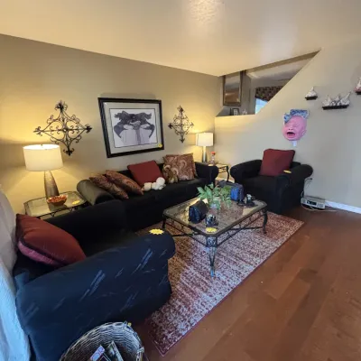Sale Photo Thumbnail #2: Living room furniture set including a black upholstered sofa and armchairs, glass-top coffee table with wrought iron frame, table lamps, framed artwork, and decorative wall art.
