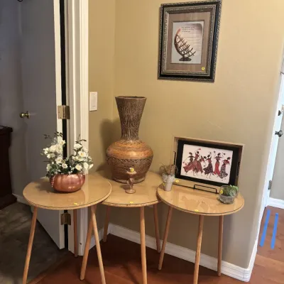 Sale Photo Thumbnail #12: Set of three modern round tripod side tables styled with decorative vases, framed artwork, and faux floral arrangements.