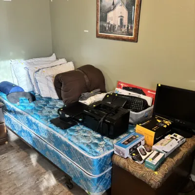 Sale Photo Thumbnail #23: Twin mattress set with bedding alongside various electronics including a computer monitor, printer, keyboards, and boxed accessories on a padded bench.