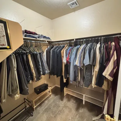 Sale Photo Thumbnail #15: Walk-in closet filled with men's clothing, including suits, button-down shirts, t-shirts, and pants, along with shoe organizers and storage shelves.